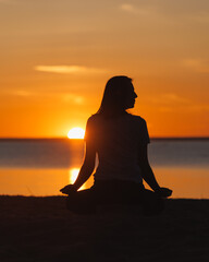 yoga meditation, silhouette of woman at sunset in lotus position. health recreation and sports, outdoor training. poster, postcard. person is engaged in breathing practices on seashore. mental health