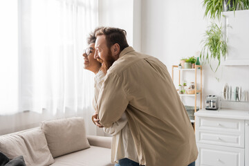 Cheerful man hugging happy african american girlfriend with curly hair at home.