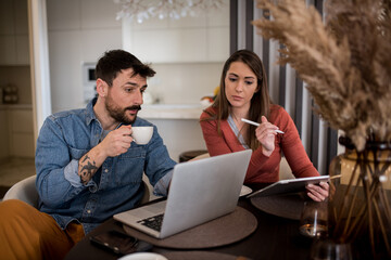 Handsome young couple working together from home, with a cup of coffee.