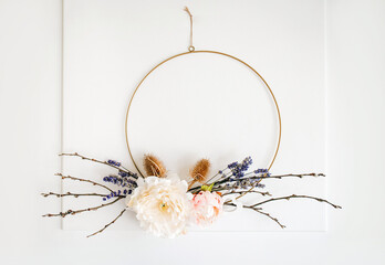 Handmade spring theme floral arrangement wreath hanging on home white door for decoration. Round metal hoop frame with various real and artificial branches and flowers attached. Catkins, lavender. 