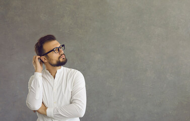 Puzzled and confused Caucasian man scratches the back of his head thinking about something important. Pensive man on a gray concrete background looks at the free space for text. Banner Advertising.