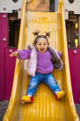 Sweet caucasian little toddler girl with two tails having fun smiling widely sliding down the...