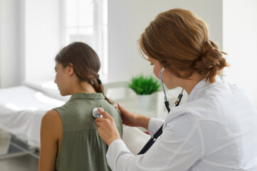 Doctor with a stethoscope examining a child patient. Female doctor in a white coat examining the...