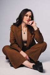 Beautiful elegant young woman model in nice stylish brown suit posing on gray background. Young...