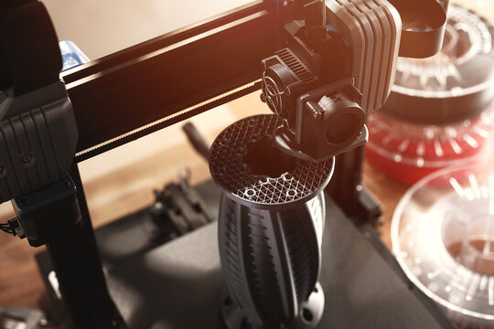 FDM-3D-printer makes a big complex flange part with internal structure from silver grey material. view on print head, infill structure and workplace. selective focus. additive manufacturing concept