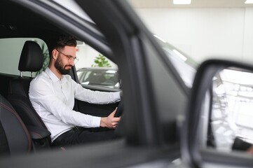 Happy caucasian man in formal wear getting inside luxury modern car for testing interior before purchase. Concept of dealership, selling and purchase