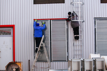 Workers installing window shutters with blinds on house or industrial building