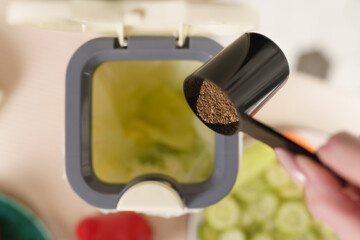 Person pouring bokashi ferment in a compost container on the table. Female recycling organic food leftovers in a composter bin with fermenting bran at home