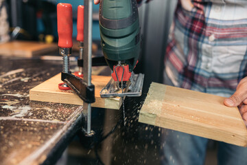 Woman cutting a wooden plank with an electric jigsaw in a workshop