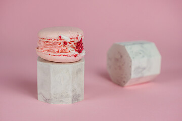Pink French macarons with cream and freeze-dried raspberries on a pink background on marble stands. A stylish concept for coffee shops, confectioners, bakeries.