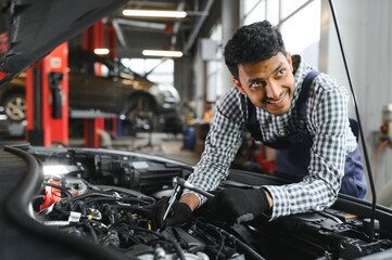 Indian car mechanic standing and working in service station. Car specialists examining the lifted car. Professional repairmen wearing mechanic uniform in blue color.