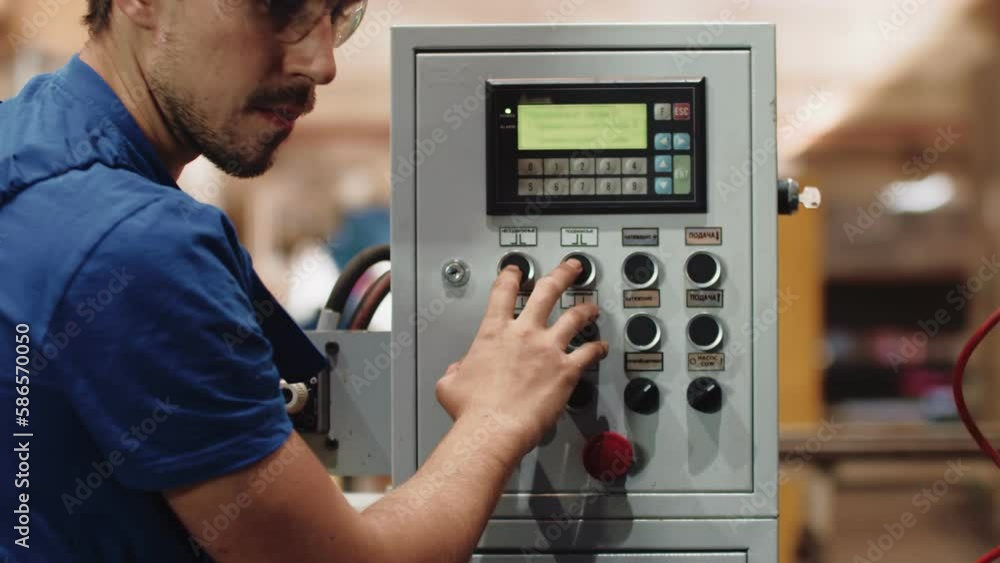 Poster Man in overalls and protective glasses presses buttons on control panel at factory, front view. Worker at the factory presses buttons on control panel