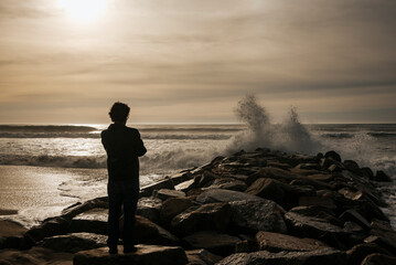 Man against cold sunset backlight. Waves crashing against the rocks on the beach. Espinho, Portugal