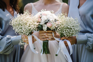 The bride and bridesmaids in an elegant dress is standing and holding hand bouquets of pastel pink...