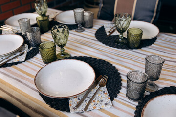 Luxury table setting for a celebration in a gazebo with greenery. Glass dishes, plates and glasses. Preparation for the holiday