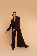 full length of young african american woman in stylish suit with wide pants posing on beige.