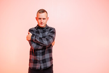 Young positive smiling man in a checkered shirt on a pink background. Place for text