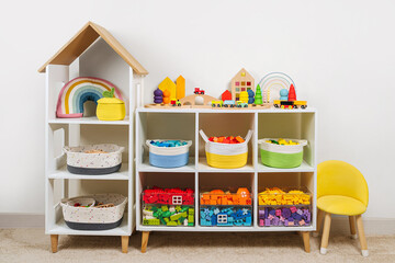 White shelving with colorful storage baskets and transparent boxes in children room. Rainbow toys...