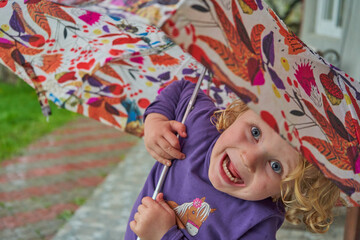 laughs a little girl under an umbrella,happy little girl hiding from the rain with an umbrella
