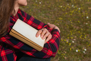 Unrecognizable woman sitting on the grass holding a book with her arms crossed