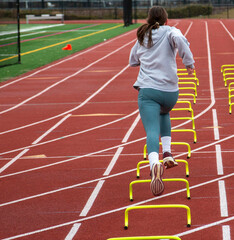 Rear view of female runner wearing spandex running over six inch mini hurdles on a track