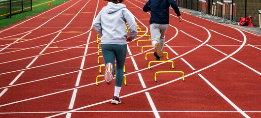 Two runners running over six iinch hurdles in lane on a track