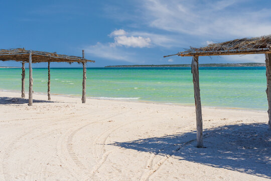 Rustic beach shelters on a white sandy beach with calm turquoise water behind