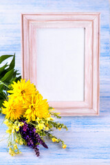 bouquet of different summer flowers and photo frame on blue background