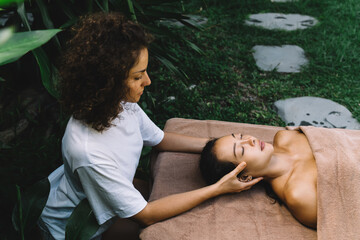 Caucasian woman in white shirt doing massage therapy to relaxed Asian client during weekend dayspa at nature, female enjoying femininity procedure for refreshing body and mind and feel vitality