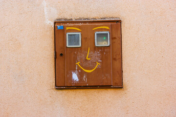 Industrial electrical junction box on the orange wall with a funny image in a form of a smiling...