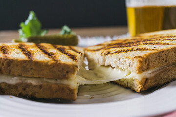 Grilled cheese sandwich cut in half. Glass of beer in the background,