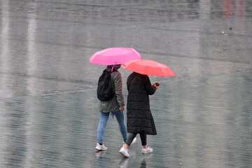 Two woman with pink orange umbrella under rain walking from back part and no face. Colorful umbrella rain autumn concept. Selective focus. Open space area.