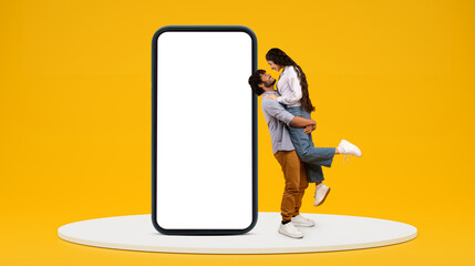 Happy millennial indian guy hold girlfriend, have fun near huge phone with blank screen