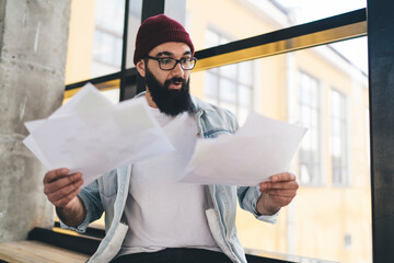 Amazed young self employed man reading documents on windowsill