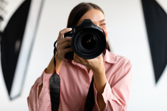 Young woman with dslr camera photographing in studio with lighting equipment, taking pictures with professional camera