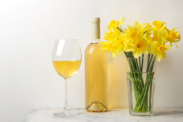 a bouquet of spring flowers daffodils in a vase and a glass of wine on a light background