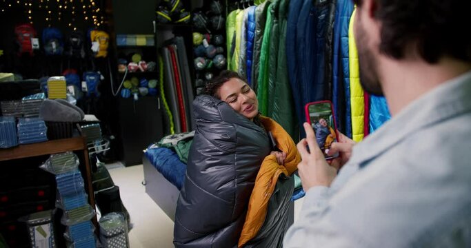 Young couple choosing sleeping bag, a man makes photo of her girlfriend
