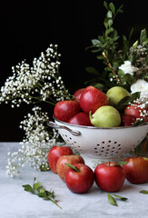 Apples and flowers on a table. Shiny red apples in a colander, Black background. 