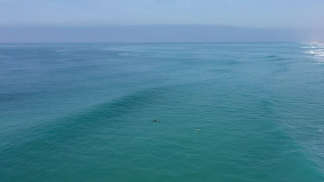 Aerial drone view of surfer sitting on his board watching the waves coming by.