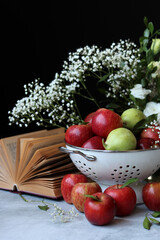 Apples and flowers on a table. Shiny red apples in a colander, Black background. 