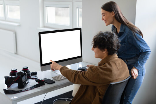 Happy young male photographer and female art director checking pictures on computer display, working together in studio