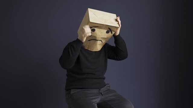 A sad man in a black turtleneck with a bag on his head, with a drawn crying emoticon, holds his head and cries. Emotions and gestures.