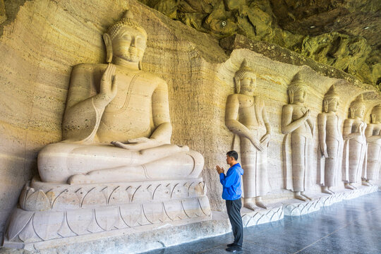 Kalasin, Thailand - February 1, 2023. Buddhist men worship a carved stone Buddha image  at Phu Dan Hai Temple, Kuchinarai District Kalasin Province, Thailand