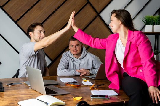 Two colleagues gives a high five, third guy sits without any attention. "Third wheel" in office.