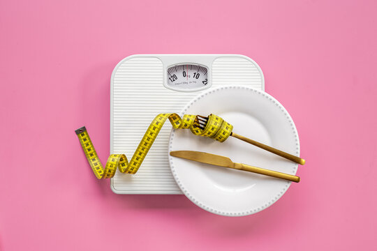 Weight scale and tape measure over dinner fork and knife on the plate