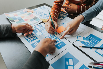 Close up ux developer and ui designer brainstorming about mobile app interface wireframe design on table with customer breif and color code at modern office.Creative digital development agency