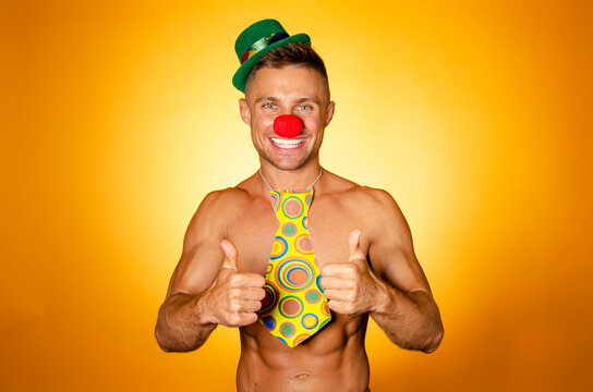 Young attractive man with an athletic body in a clown costume. Orange background.