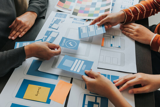 Close up ux developer and ui designer brainstorming about mobile app interface wireframe design on table with customer breif and color code at modern office.Creative digital development agency