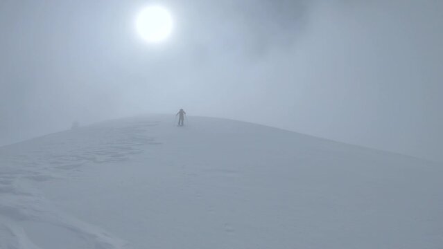 man hiking on splitboard cloudy landscape sun winter high mountain.