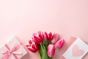 Mother's Day atmosphere concept. Top view photo of bouquet of fresh tulips big present box and pink envelope with postcard on isolated pastel pink background with copyspace